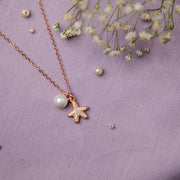 A rose gold-colored silver pendant chain with a starfish motif and a pearl, displayed on a purple background with some scattered flower petals.